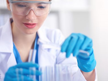 Kadın araştırmacı, beyaz arka planda izole edilmiş ilaç şişeleri ve mataralarla çevrili.