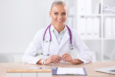 Güzel, genç, gülümseyen bayan doktor masada oturuyor ve yazıyor..