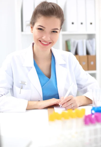 Bonito jovem sorridente médico feminino sentado na mesa . — Fotografia de Stock