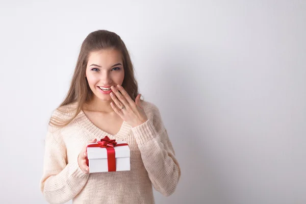 年轻女人幸福的微笑举行礼品盒在手中，站在灰色背景 — 图库照片