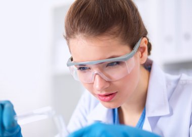 Kadın araştırmacı, beyaz arka planda izole edilmiş ilaç şişeleri ve mataralarla çevrili.