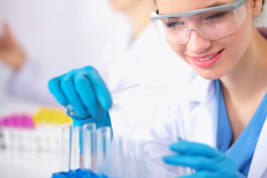 Kadın araştırmacı, beyaz arka planda izole edilmiş ilaç şişeleri ve mataralarla çevrili.