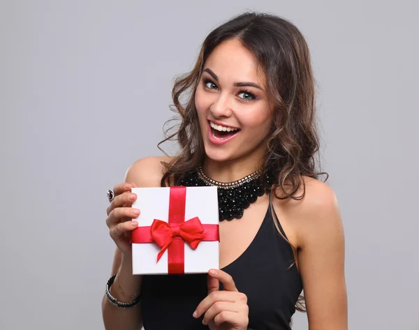 Ung kvinna lyckligt leende hålla presentförpackning i händer, isolerade på grå bakgrund — Stockfoto