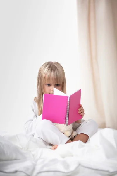 작은 여 자가 침대에 누워 책을 읽고 — 스톡 사진