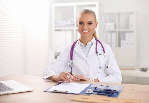 美しい若い笑顔の女性医師が机に座って書きます. — ストック写真