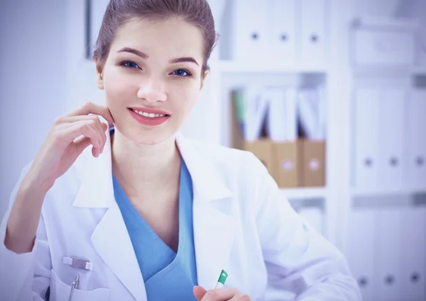 Hermosa joven sonriente doctora sentada en el escritorio . — Foto de Stock