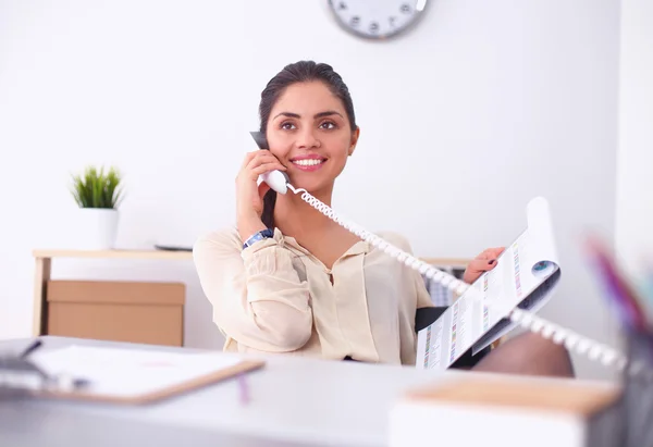 Jovem empresária sentada na mesa e conversando ao telefone — Fotografia de Stock