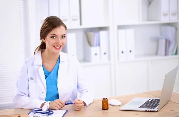 Doctora sentada en el escritorio y trabajando en un portátil — Foto de Stock