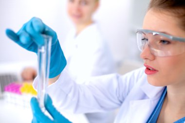 Kadın araştırmacı, beyaz arka planda izole edilmiş ilaç şişeleri ve mataralarla çevrili.