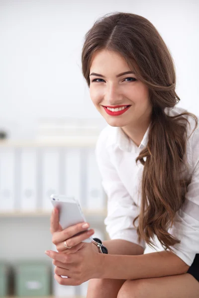 Businesswoman sending message with smartphone sitting in the office — Stock Photo, Image