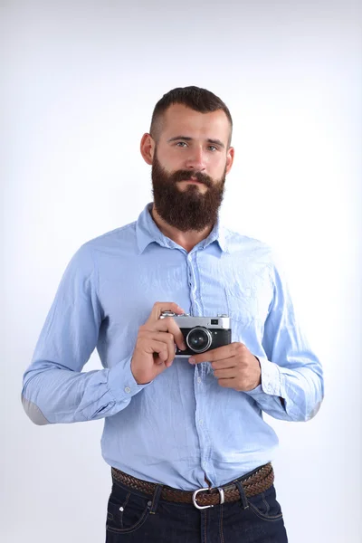 Joven barba hombre sosteniendo una cámara mientras está de pie sobre fondo blanco — Foto de Stock