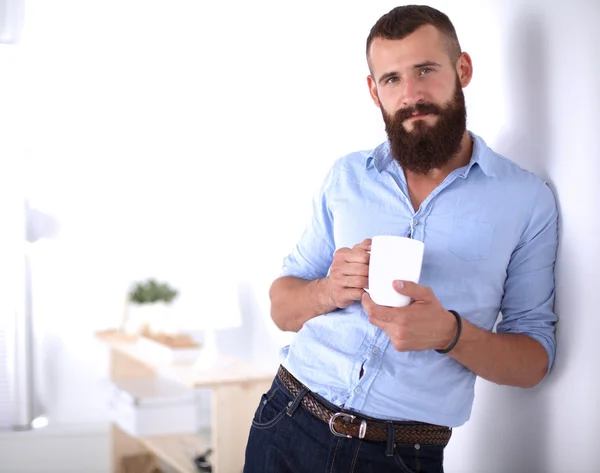Jonge man permanent in de buurt van muur en houden kopje koffie in office — Stockfoto