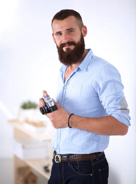 Joven barba hombre sosteniendo una cámara mientras está de pie sobre fondo blanco — Foto de Stock