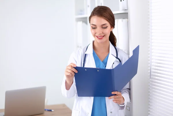 Médico sonriente con una carpeta en uniforme de pie en el hospital — Foto de Stock