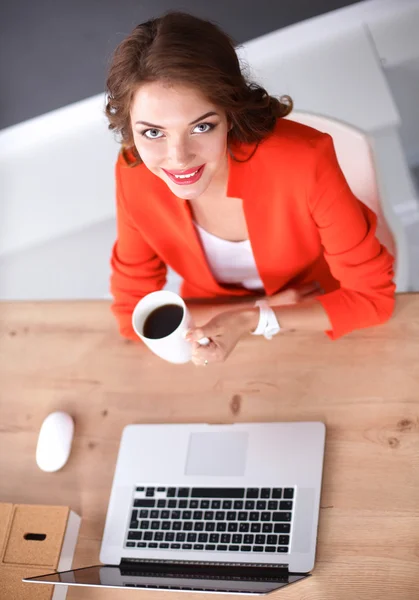 Привлекательная женщина сидит за столом в офисе, работает с ноутбуком — стоковое фото
