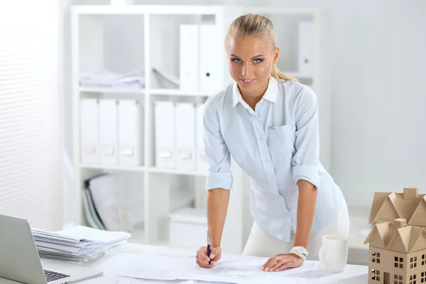 Portrait of female architect with blueprints at desk in office — Stock Photo, Image