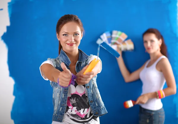 Dos mujeres hermosas jóvenes sosteniendo la paleta de colores, de pie cerca de la pared . —  Fotos de Stock