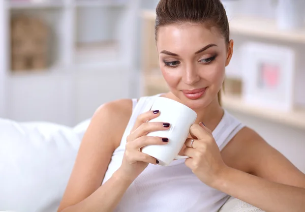 Young beautiful woman with a cup on sofa at home — Stock Photo, Image