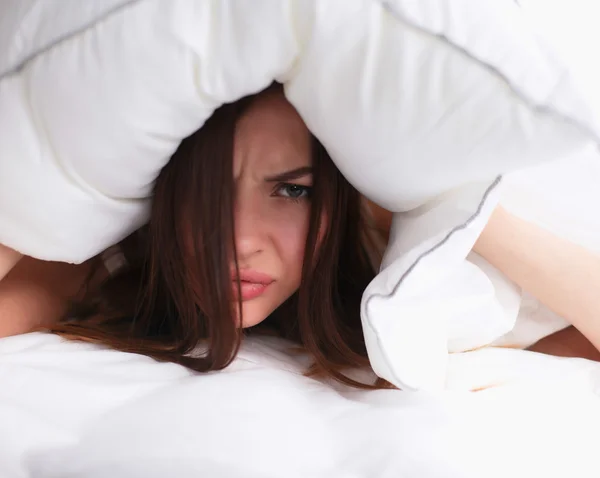 Жінка лежить на ліжку і закриває вуха подушкою — стокове фото