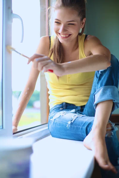 Woman with a paintbrush carefully finishing off around a window frame — Stock Photo, Image