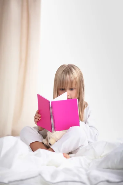 Küçük kız yatakta yatan ve bir kitap okuma — Stok fotoğraf