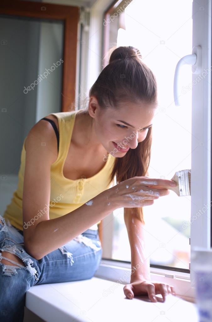 Woman painting wall of an apartment with a paintbrush carefully finishing off around  window frame