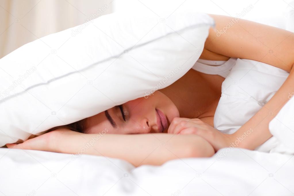 Female lying on bed and closing her ears with pillow