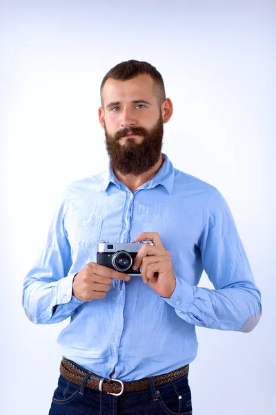 Молодой бородач держит камеру, стоя на белом фоне — стоковое фото