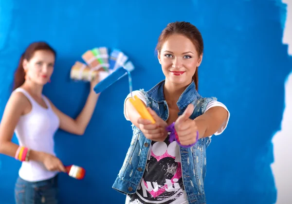 Dos mujeres hermosas jóvenes sosteniendo la paleta de colores, de pie cerca de la pared . —  Fotos de Stock