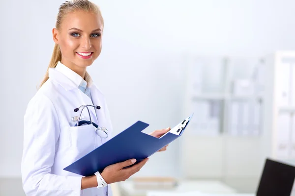 Médico sonriente con una carpeta en uniforme de pie en el hospital —  Fotos de Stock