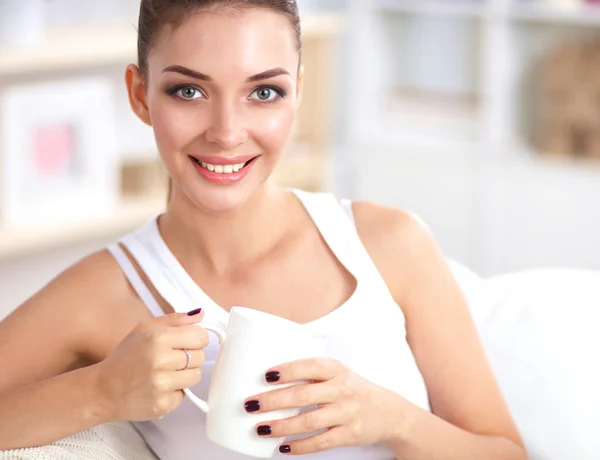 Portrait of oung beautiful woman with a cup on sofa at home — Stock Photo, Image