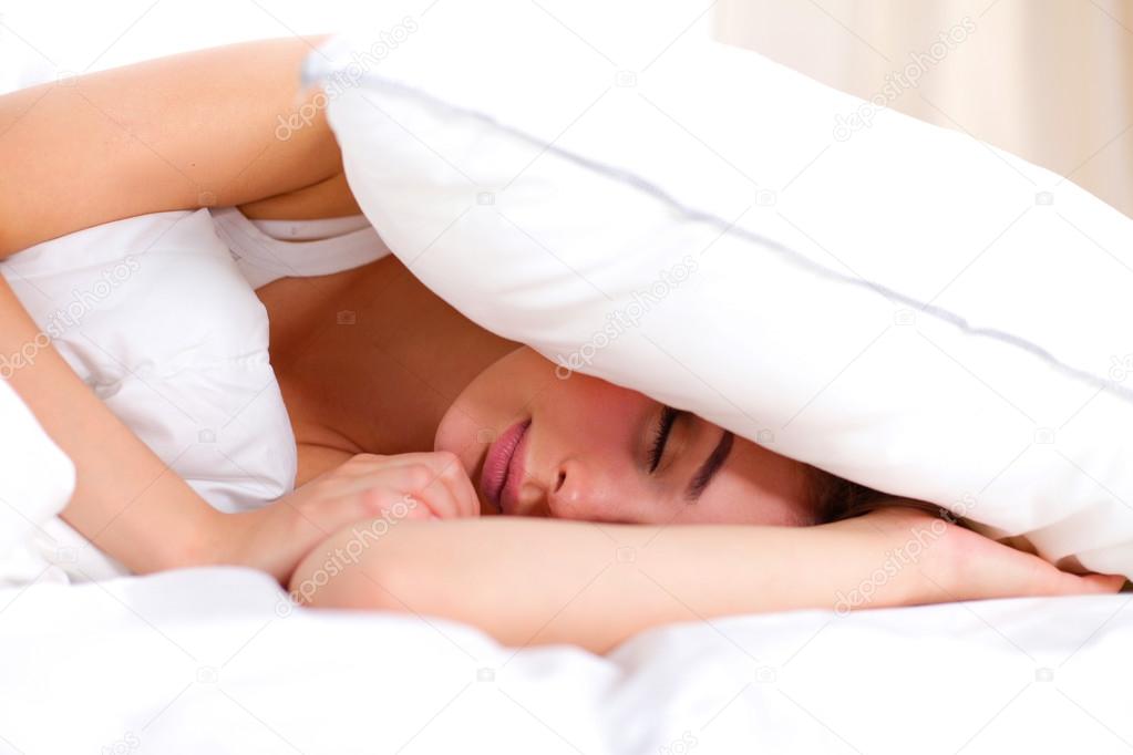 Female lying on bed and closing her ears with pillow