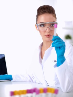 Kadın araştırmacı, beyaz arka planda izole edilmiş ilaç şişeleri ve mataralarla çevrili.