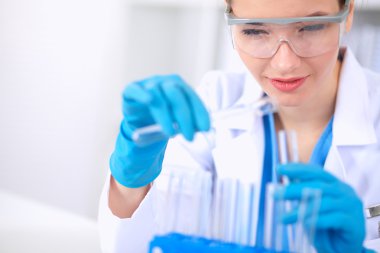 Kadın araştırmacı, beyaz arka planda izole edilmiş ilaç şişeleri ve mataralarla çevrili.