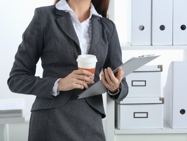 Çekici genç iş kadını masanın yanında elinde dosyayla duruyor.