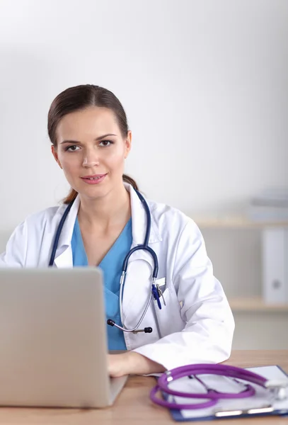 Belle jeune femme médecin souriante assise au bureau et écrivant. — Photo