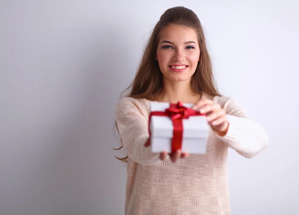 Jonge vrouw gelukkig glimlach houden de doos van de gift in handen, permanent over grijze achtergrond — Stockfoto