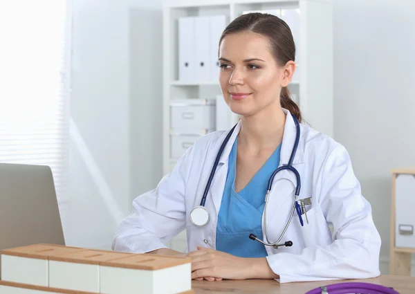 Mooie jonge glimlachende vrouwelijke arts zitten aan het bureau en schrijven. — Stockfoto