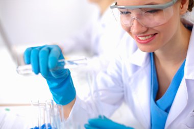 Kadın araştırmacı, beyaz arka planda izole edilmiş ilaç şişeleri ve mataralarla çevrili.