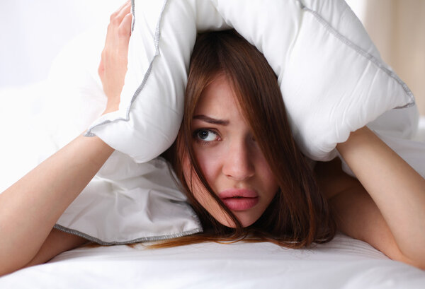 Female lying on bed and closing her ears with pillow
