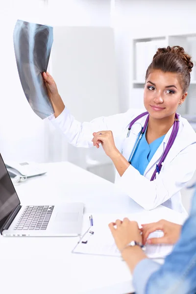 Doctora joven estudiando imagen de rayos X sentada en el escritorio —  Fotos de Stock