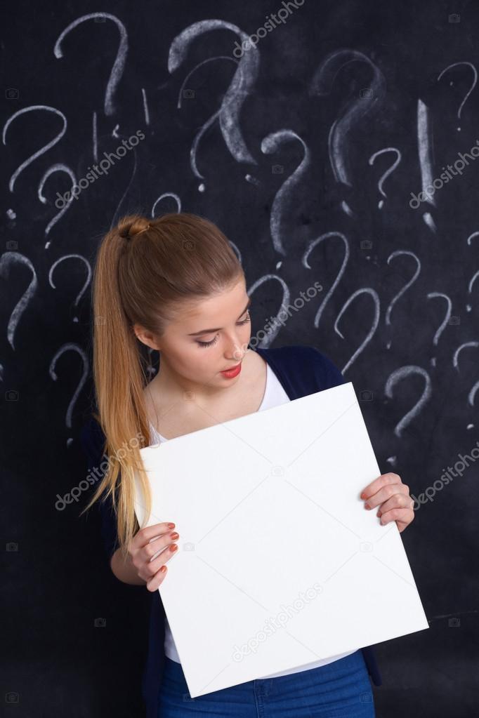 Young girl with question mark holding a blank on  gray background