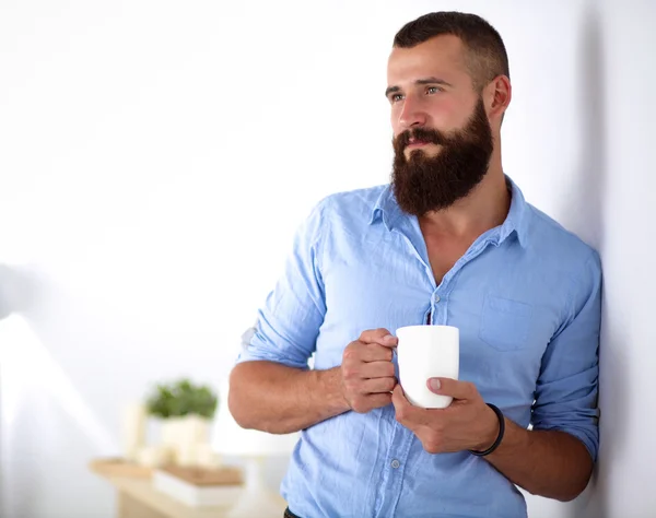 Jonge man permanent in de buurt van muur en houden kopje koffie in office — Stockfoto