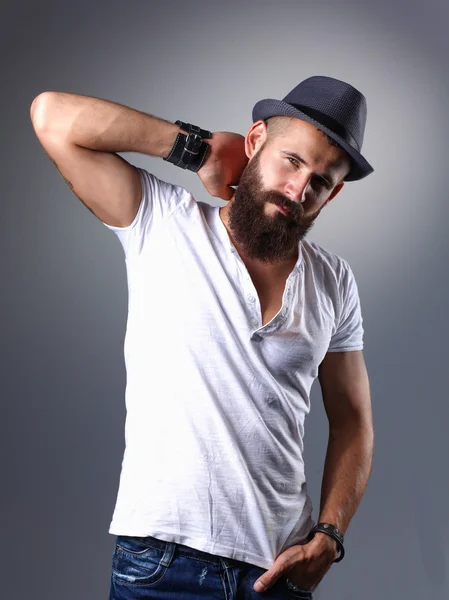 Portrait of handsome bearded man in hat standing , isolated on grey background — Stock Photo, Image