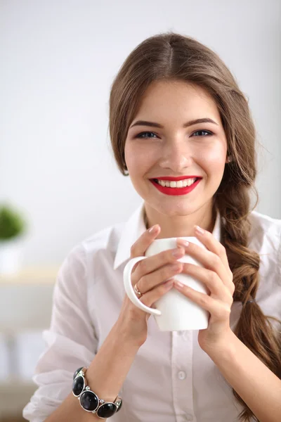 Jonge zakenvrouw zit op het bureau met beker in het kantoor — Stockfoto