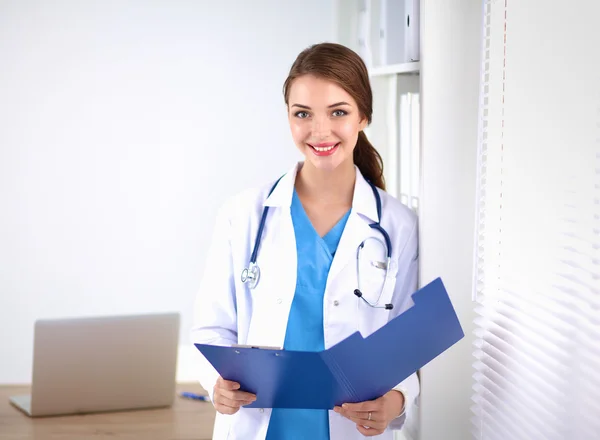 Sorridente medico donna con una cartella in uniforme in piedi in ospedale — Foto Stock