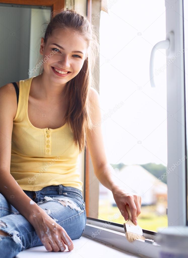 Woman painting wall of an apartment with a paintbrush carefully finishing off around  window frame