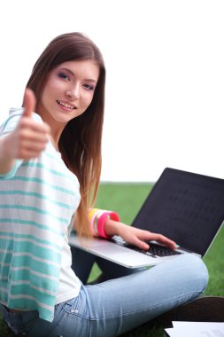 Laptoplu genç bir kadın yeşil çimlerde oturuyor. 