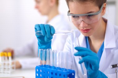 Kadın araştırmacı, beyaz arka planda izole edilmiş ilaç şişeleri ve mataralarla çevrili.