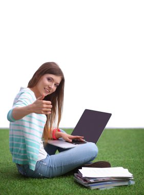 Laptoplu genç bir kadın yeşil çimlerde oturuyor. 